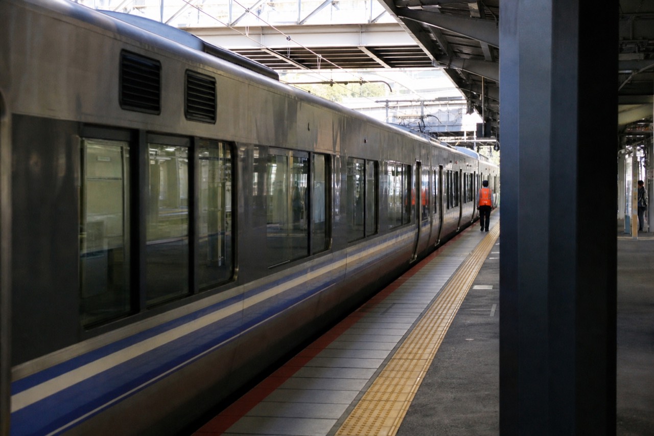 A train platform in Kyoto with a rapid service train stopped beside the yellow platform line