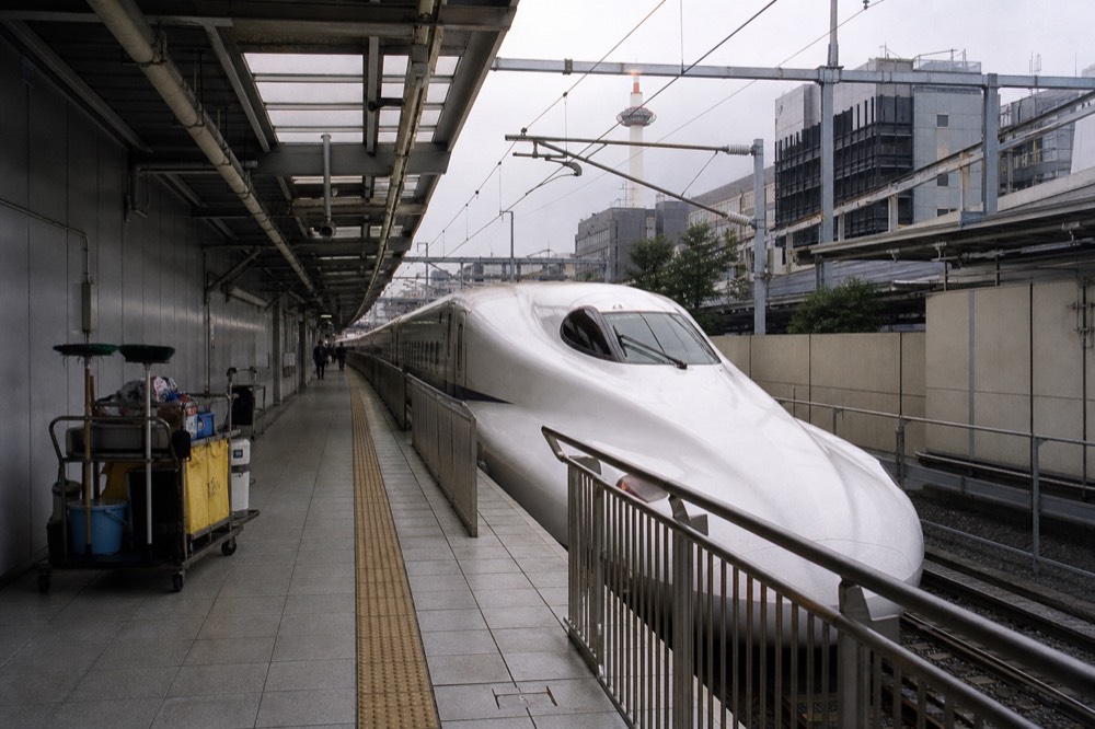 A bullet train platform with a long white train at rest beside a station sign
