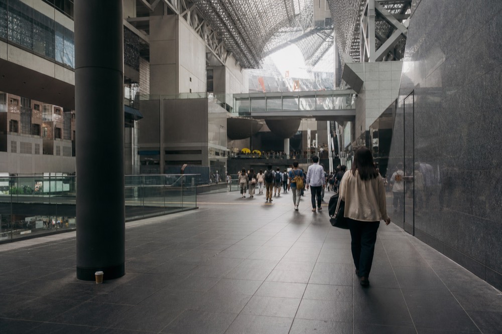 A wide station concourse with departure boards and travellers walking between platforms