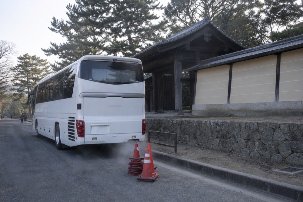 A tour coach parked on a street beside old temple buildings in Nara