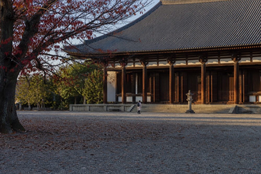A large wooden temple hall with a tiled roof seen across an open courtyard