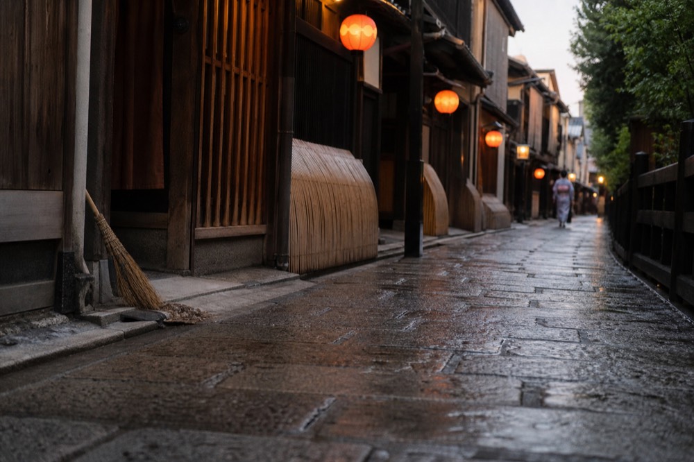 A stone lane in Gion with wooden lattice facades, hanging lanterns and evening light on the pavement