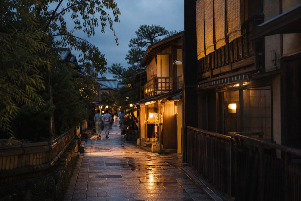 Warm light on wooden teahouse balconies and stone paving in a Kyoto geisha district in the evening