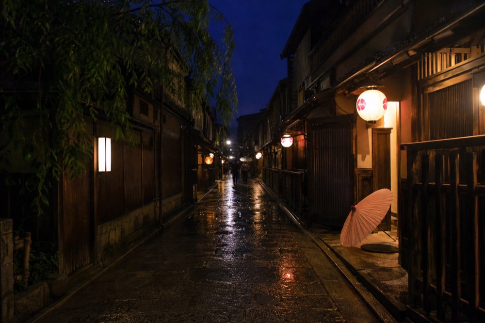 A quiet lane of traditional wooden buildings with paper lanterns glowing against a darkening sky