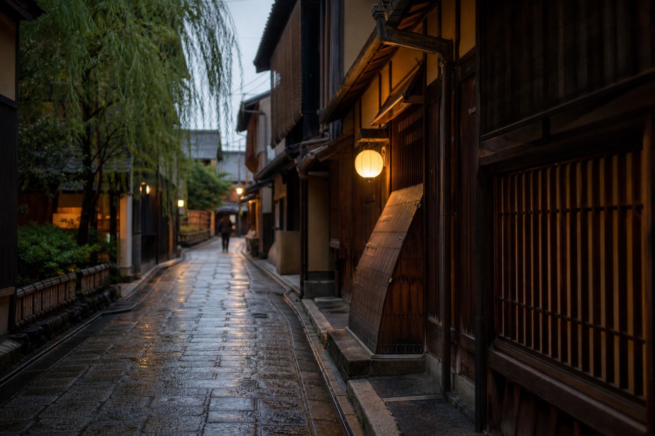 A narrow stone-paved alley lined with traditional wooden machiya facades and paper lanterns in the early evening