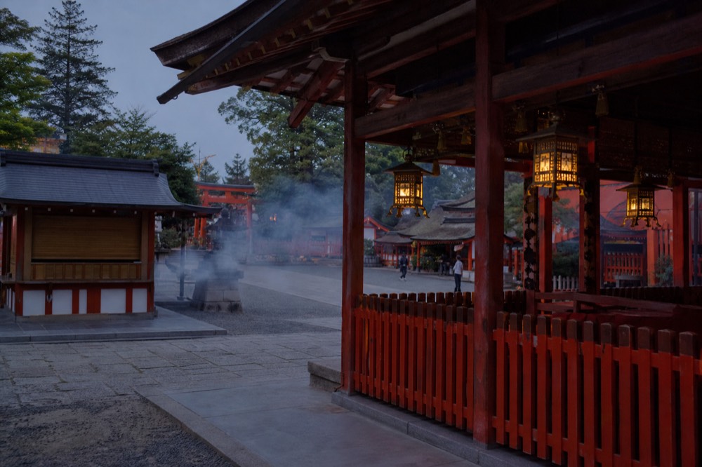 The main shrine buildings of Fushimi Inari with lanterns hanging under the eaves at dusk