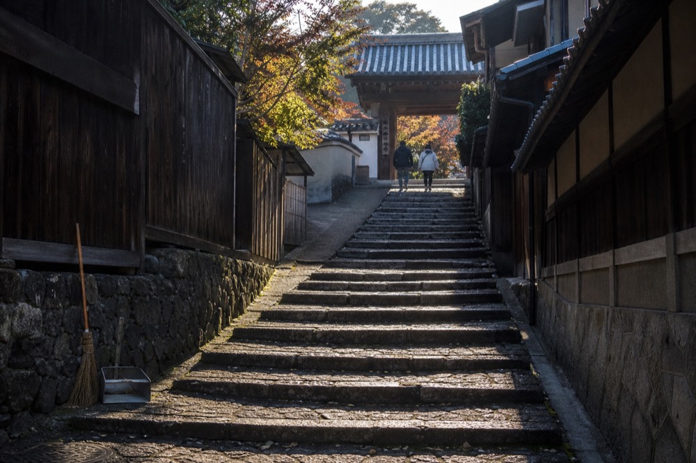 Stone steps climbing a narrow lane between wooden houses toward a temple gate in Kyoto