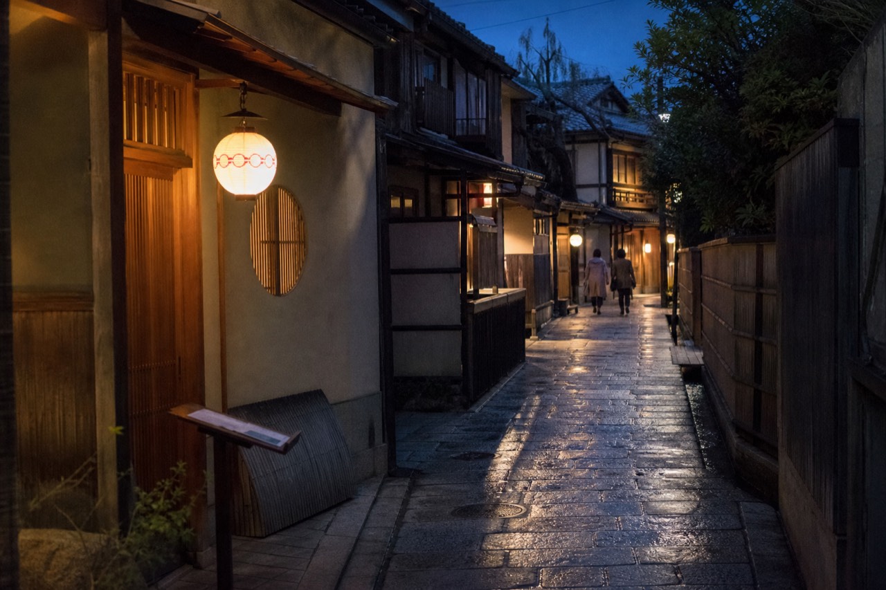 A narrow Kyoto street with traditional wooden machiya facades and lanterns at dusk