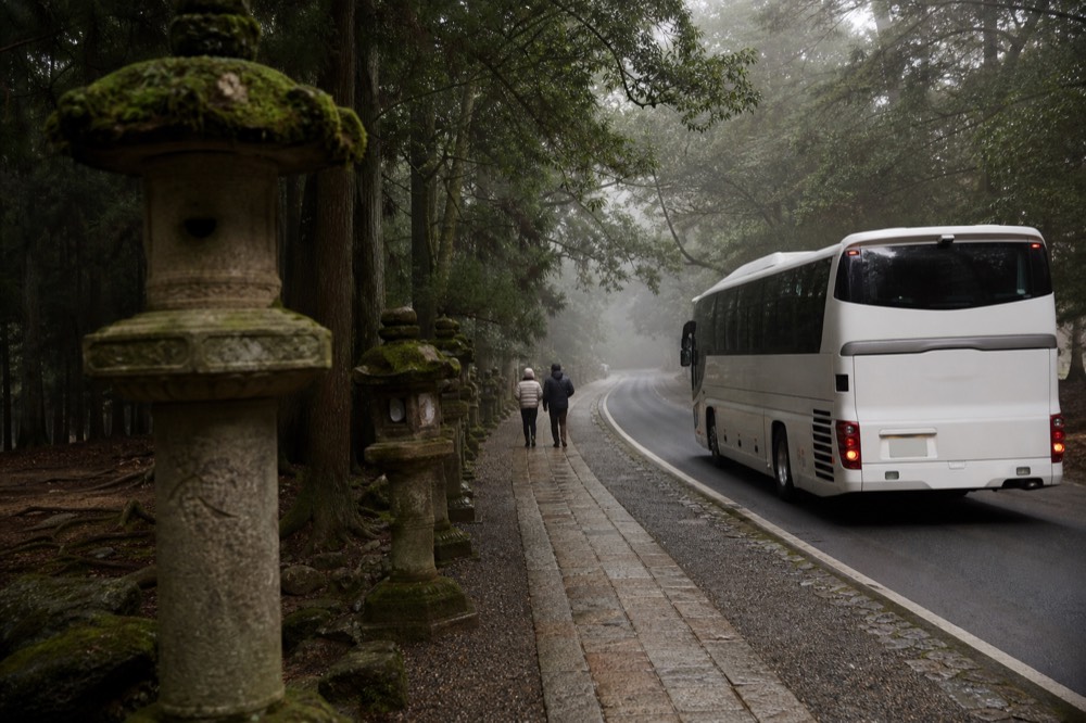Tour coach parked beside a stone lantern at a shrine approach