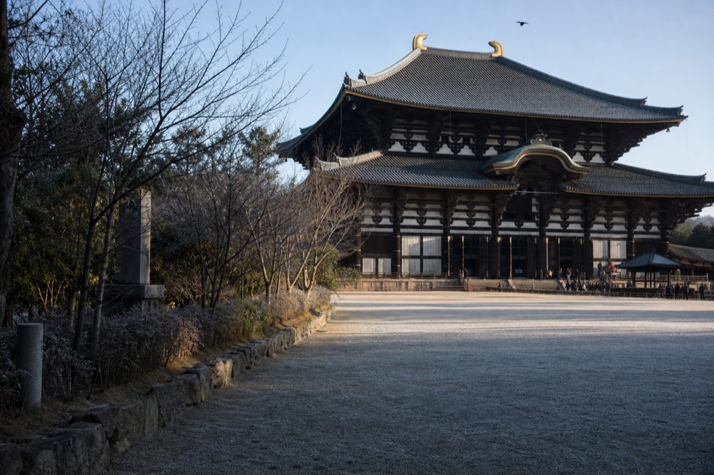 A great wooden temple hall seen across a wide gravel courtyard