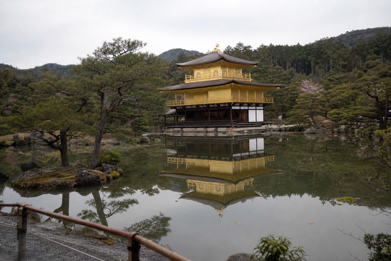 The gold-leafed pavilion of Kinkaku-ji reflected in the still Mirror Pond with pine trees along the shore
