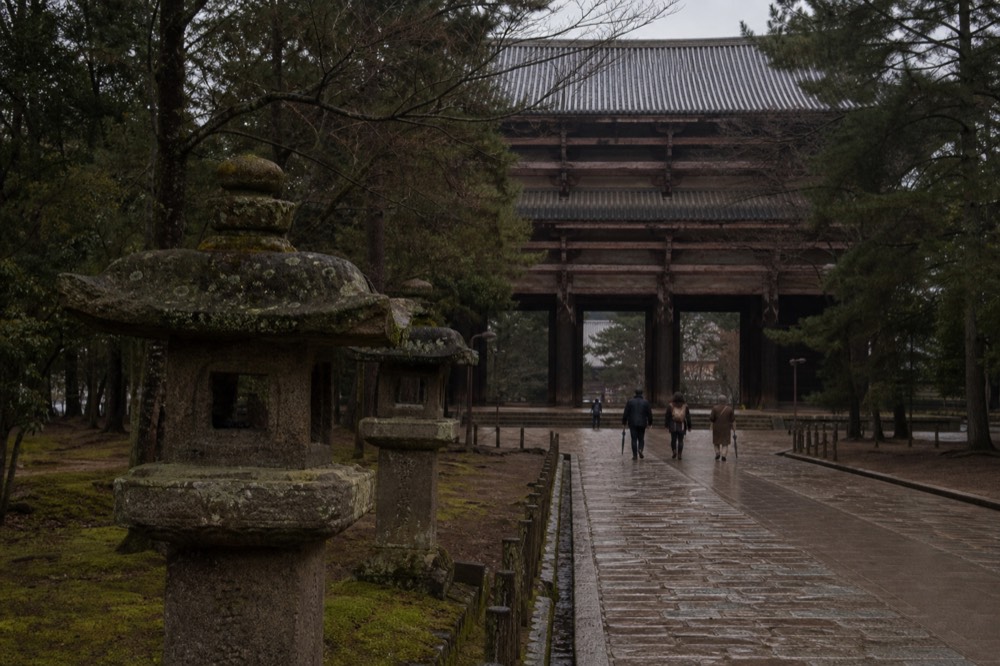 Stone lanterns and a stone path leading toward a large temple gate