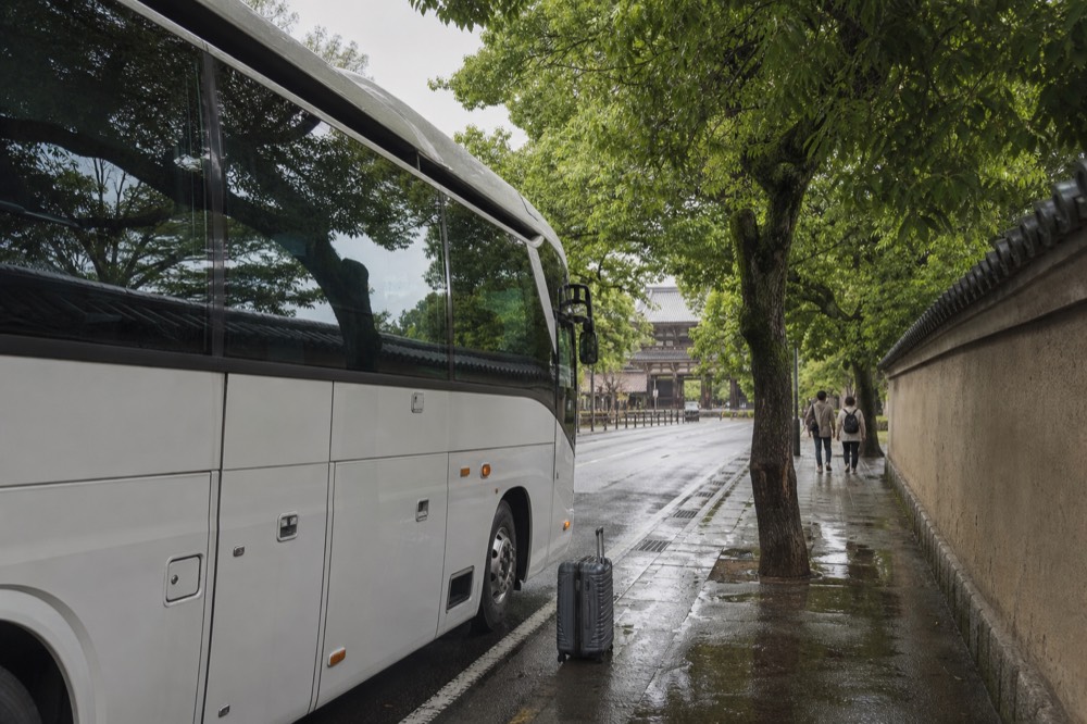 A sightseeing coach parked beside a tree-lined street near temple grounds