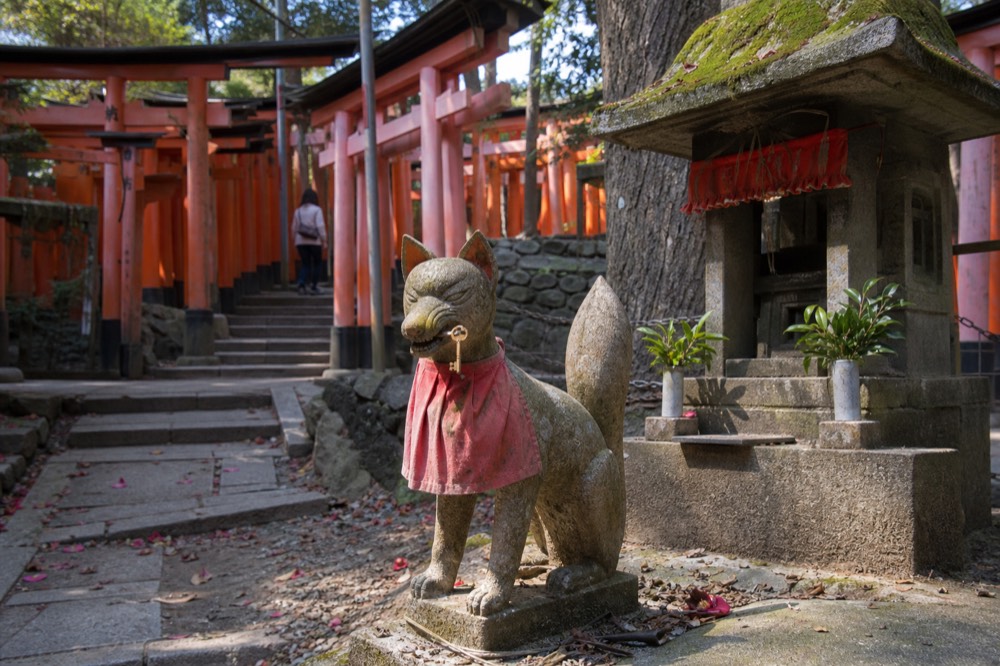 A fox statue holding a key in its mouth in front of a small shrine building