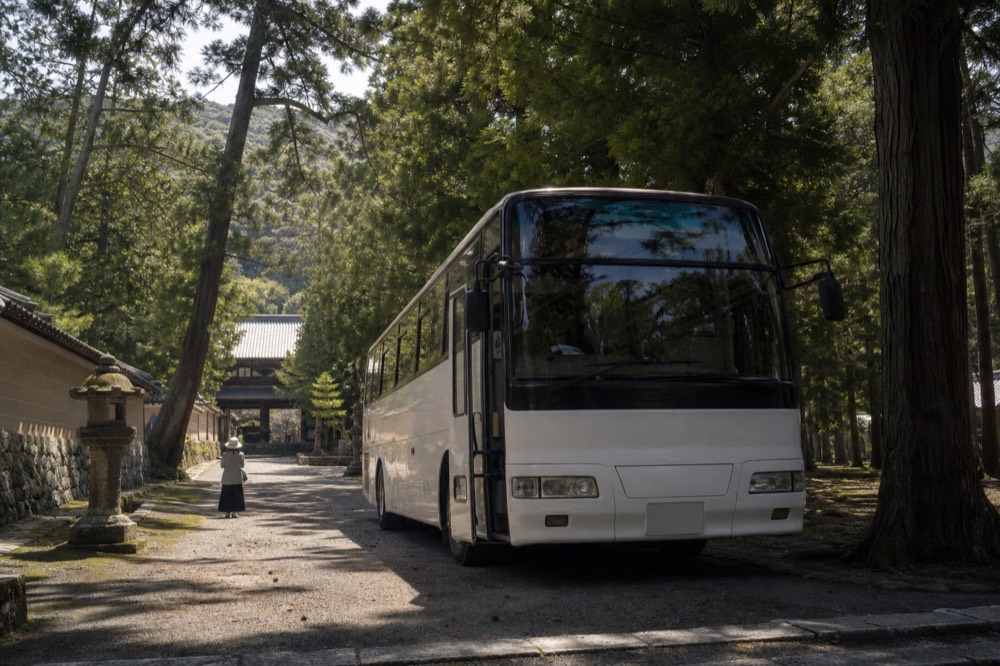 A tour coach parked on a tree-lined road near temple grounds