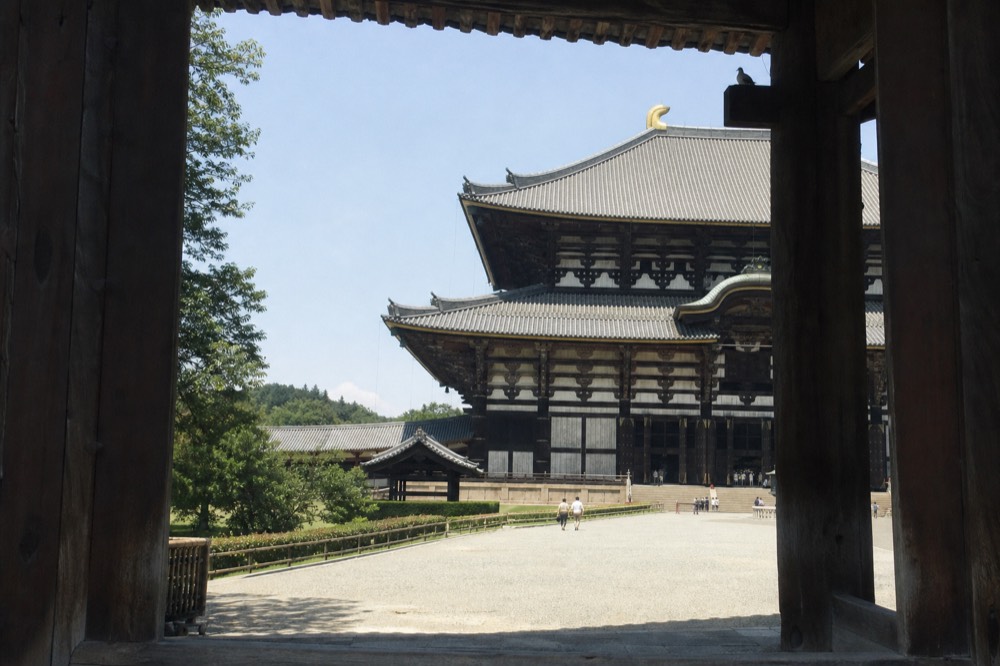 A large wooden temple hall with a tiled roof seen across an open courtyard