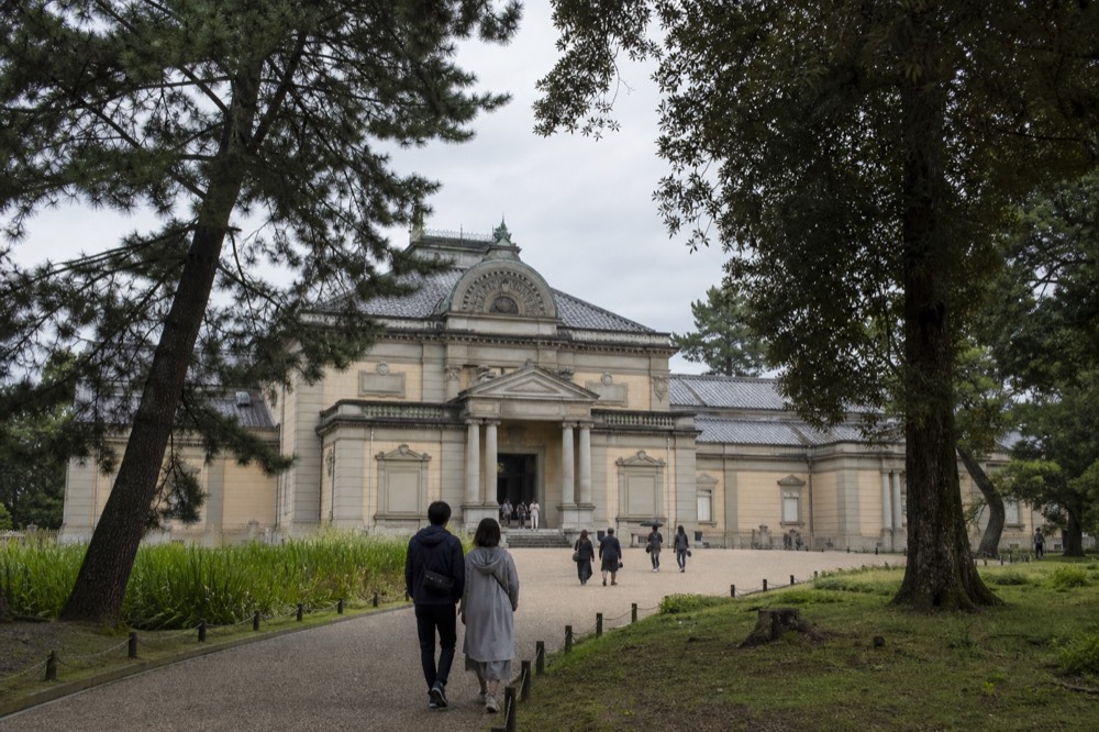 A red brick Meiji era museum building with a steep roof seen across a lawn