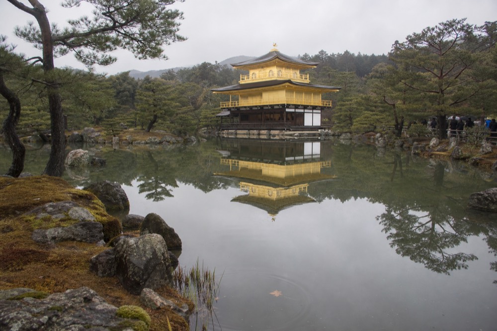 A golden pavilion reflected in a still pond surrounded by pine trees