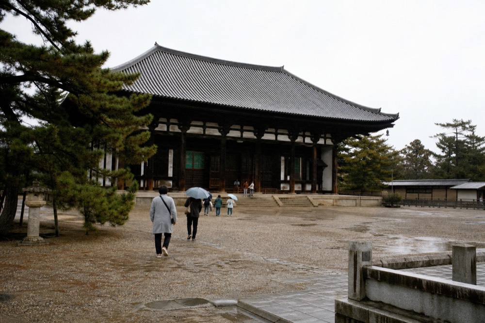 A wooden temple hall with a large tiled roof seen across an open courtyard