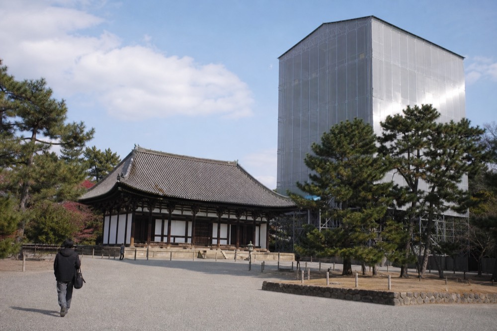 A temple hall with a tiled roof beside a tall steel enclosure