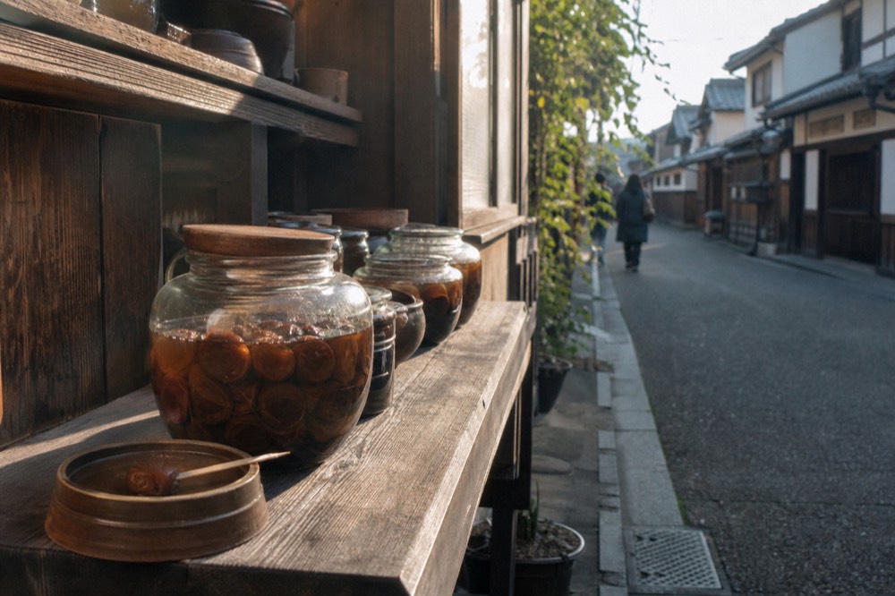 Glass jars of dark pickled vegetables on a wooden shop shelf