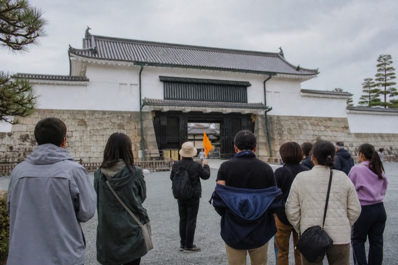 An English-speaking guide addressing coach travellers outside a historic Kyoto gate
